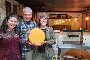 Three people in a Colombian restaurant holding a wheel of cheese
