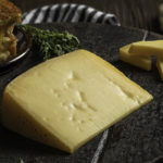 a wedge of Galen's Good Old gouda cheese with a grilled cheese sandwich in the background