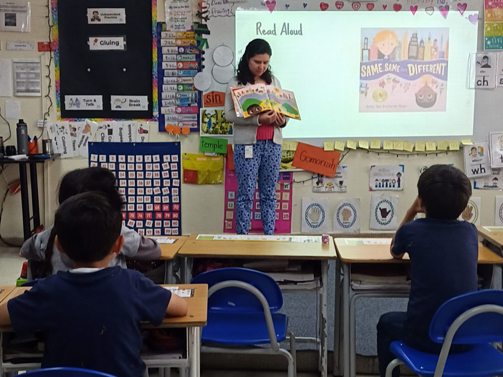 A teacher reading from a book in front of a classroom