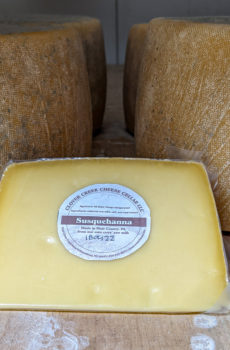 a wedge of cheese with cheese wheels in the background