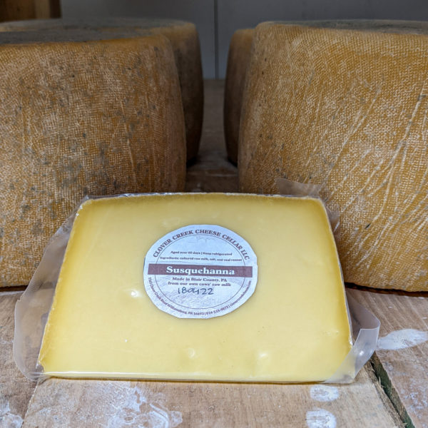 a wedge of cheese with cheese wheels in the background